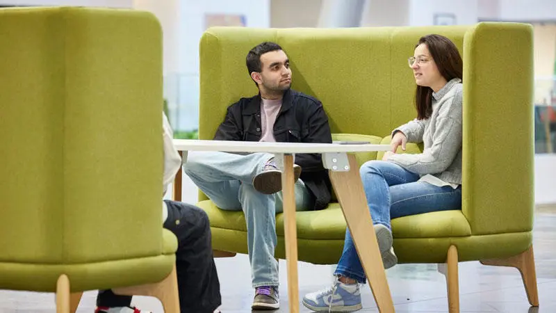 Two students sat on a green sofa