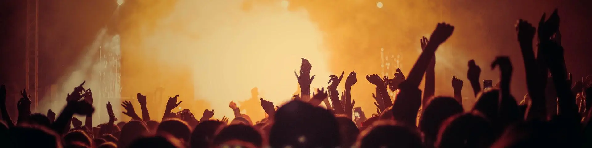 Young people dance in a club with hands in the air. They are in the foreground in front of an illuminated stage.