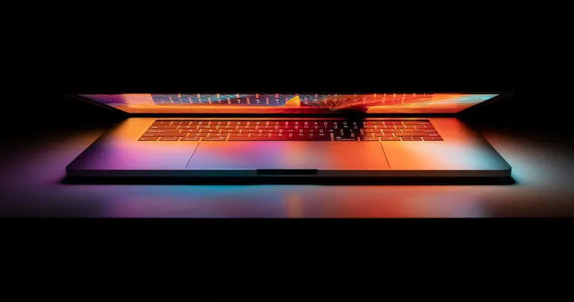 A partially closed laptop with a lit screen shining on the keyboard. 